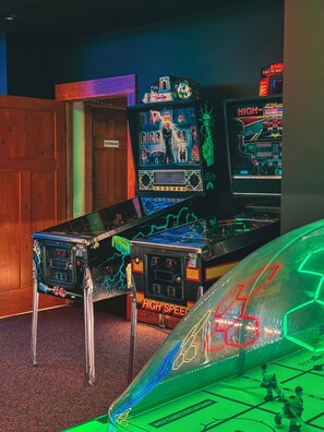 A room with arcade games, including a pinball machine and a racing game.