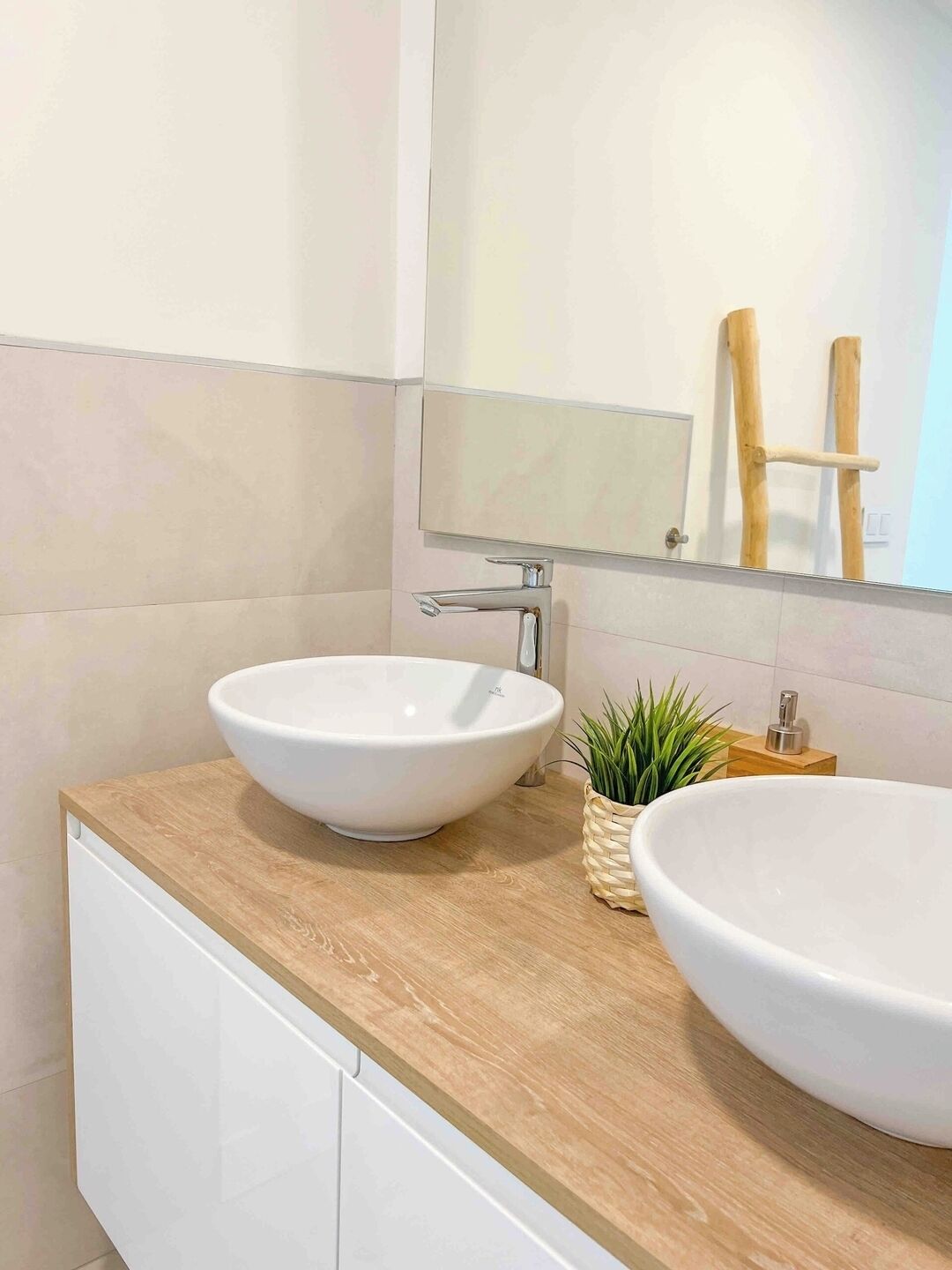 A bathroom with two white vessel sinks on a wooden countertop, a small potted plant, and a mirror above.