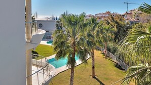Zona de piscina con palmeras, cielo despejado y vistas de edificios circundantes.