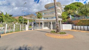 Un edificio moderno con fachada curva, una palmera en el centro y una entrada cercada.