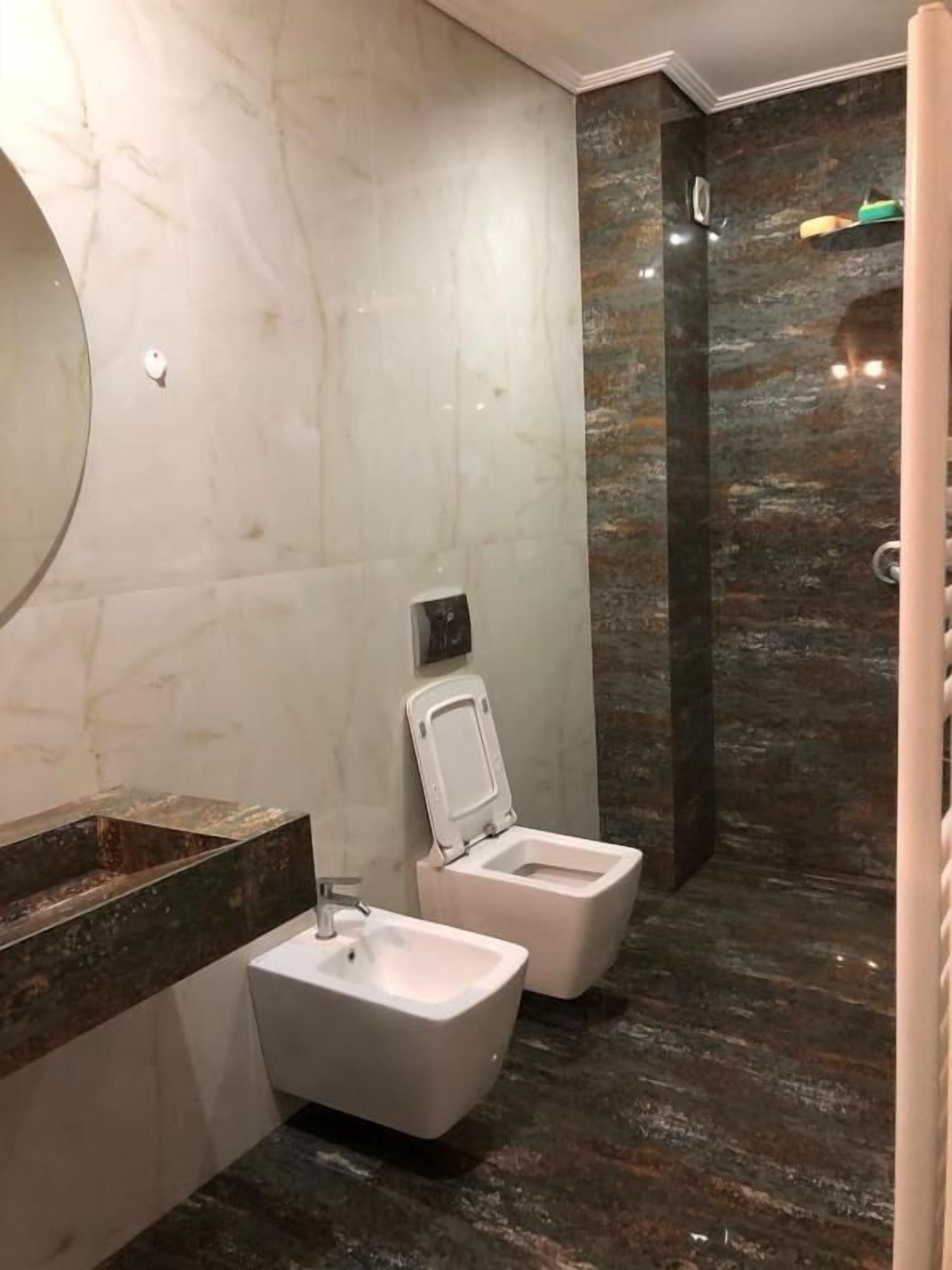 Ein modernes Badezimmer mit Waschtisch aus Marmor, zwei Toiletten und einer Duschkabine.