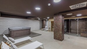 Ett modernt spaområde med ett bubbelbad, solstolar och en pelare dekorerad med mosaik.