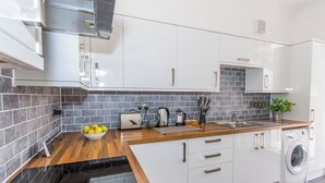 A modern kitchen with white cabinets, a wooden countertop, a built-in washing machine, and a tiled backsplash. - Spacious 3 bed apartment near RWY in Plymouth (Cremyll)