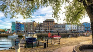 A waterfront promenade with historic buildings, a dock with boats, and a paved walkway. - Spacious 3 bed apartment near RWY in Plymouth (Cremyll)
