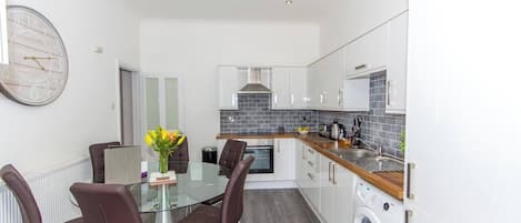 A modern kitchen with a glass dining table, brown chairs, and a built-in washing machine.