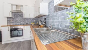 A modern kitchen with a built-in oven, stainless steel sink, and grey tiled backsplash. - Spacious 3 bed apartment near RWY in Plymouth (Cremyll)