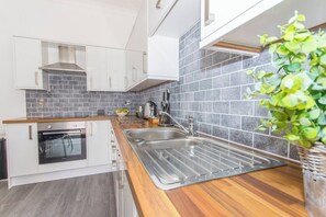 A modern kitchen with a built-in oven, stainless steel sink, and grey tiled backsplash. - Spacious 3 bed apartment near RWY in Plymouth (Cremyll)