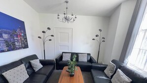 A modern living room with a black leather sofa set, a wooden coffee table, and a cityscape painting on the wall.
