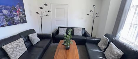 Una sala de estar moderna con un sofá de cuero negro, una mesa de centro de madera y un cuadro con vista a la ciudad.