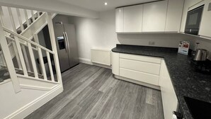 A modern kitchen with white cabinetry, a black countertop, and a grey wooden floor.