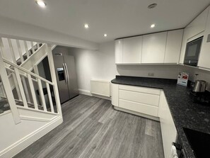 A modern kitchen with white cabinetry, a black countertop, and a grey wooden floor. - Luxury 4 bedroom ground floor apartment (Plymouth)