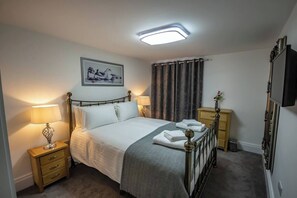 A neatly arranged bedroom with a bed, bedside lamps, a flat-screen TV, and a framed picture on the wall. - 2 Bed - The Sandringham Suite by Smart Welcomes (Plymouth)