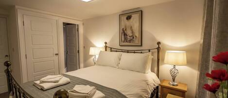 A neatly made bed with white linens, a bedside lamp, and a framed artwork on the wall.