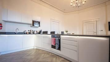Una cocina moderna con armarios blancos, horno empotrado y suelo de madera con diseño en espiga.