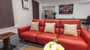 A red leather sofa with patterned cushions, a wooden coffee table, a clock, and a painting on the wall.