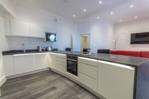 Eine moderne Küche mit Einbauofen, Spüle und Mikrowelle. Es gibt eine Sitzecke mit roten Stühlen und einem Wand-Fernseher.