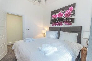 A hotel room with a bed, a nightstand, a lamp, and a door.