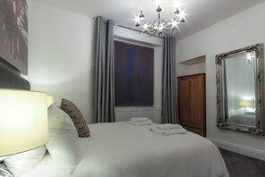 Une chambre d’hôtel avec un lit, un lustre, une fenêtre avec des rideaux, un miroir et une armoire.