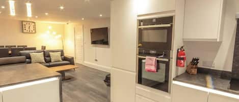 A modern kitchen with built-in appliances, a dining area with a sofa, and a flat-screen TV mounted on the wall.