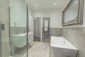 Une salle de bain moderne dotée d’une douche à parois de verre, d’une baignoire sur pieds et d’un grand miroir encadré d’un cadre orné.