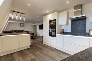 A modern kitchen with white cabinetry, a built-in oven, and a stainless steel range hood. - 3 Bed - The Regency Suite by Pureserviced (Plymouth)