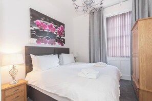 Une chambre d’hôtel avec un lit, une table de chevet, une lampe, une armoire, une fenêtre avec des rideaux et un tableau au mur.