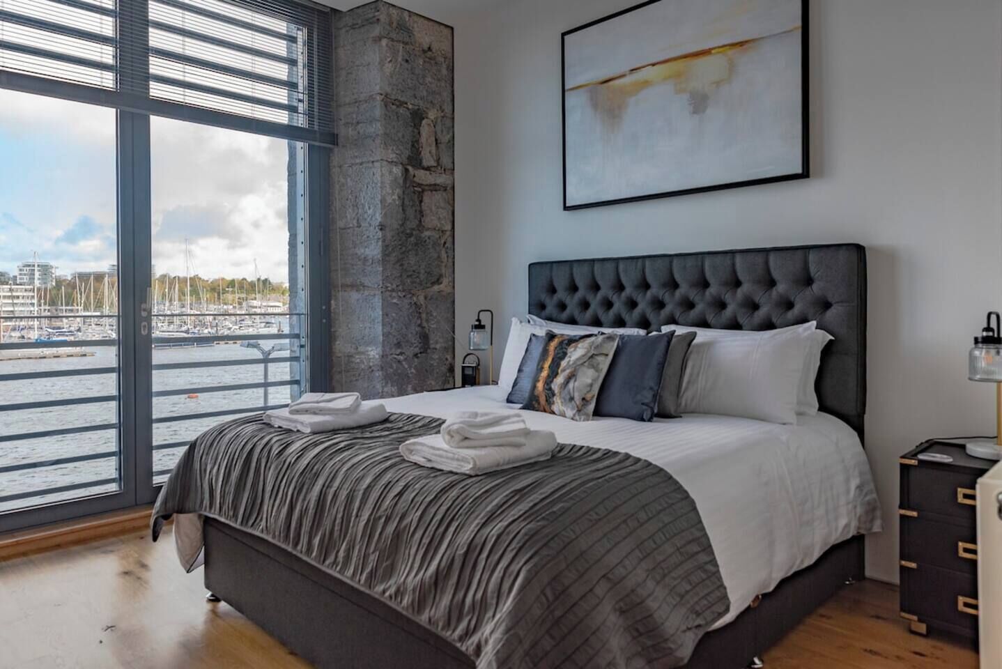 A bedroom with a large bed, a view of the water, and a modern abstract painting.