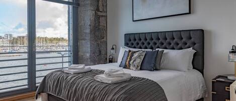 A bedroom with a large bed, a view of the water, and a modern abstract painting.