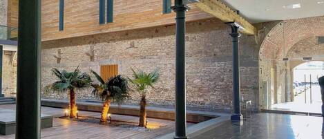 An indoor atrium with a high ceiling, stone walls, and a wooden floor.