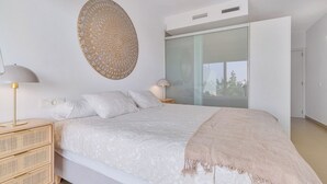 A modern bedroom with a large bed, two bedside tables, a wall-mounted decorative piece, and a sliding glass door leading to a balcony. - Stylish apartment with oceanview (Málaga)