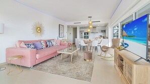 A modern living room with a pink sofa, a coffee table, and a TV displaying a beach scene. - Stylish apartment with oceanview (Málaga)