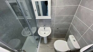 A bathroom with a glass shower enclosure, a pedestal sink, and a toilet.