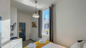 Ein Hotelzimmer mit Bett, einem Fenster mit Vorhängen, einem Heizkörper und einer Tür.