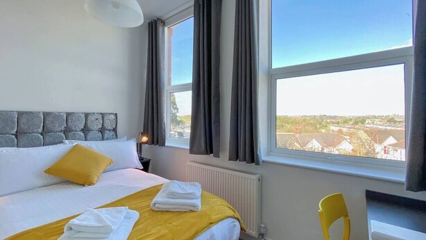 A hotel room with a large bed, a chair, a window with curtains, and a view of the outside.