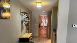A narrow hallway with a wooden door at the end, a small table with a bench, and a wall-mounted coat rack with hanging items. - Charming Mountain Studio/ Walk to the Lifts (Keystone)