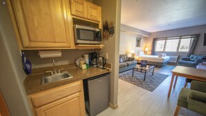 A compact kitchen with a microwave, sink, and dishwasher. There is a dining area with a table and chairs, and a living room with a sofa and a small coffee table. - Charming Mountain Studio/ Walk to the Lifts (Keystone)