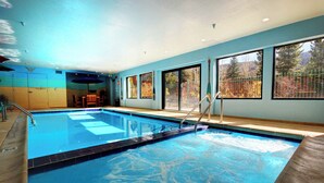 An indoor swimming pool with clear water, a wooden deck, and large windows offering views of trees and mountains. - Charming Mountain Studio/ Walk to the Lifts (Keystone)