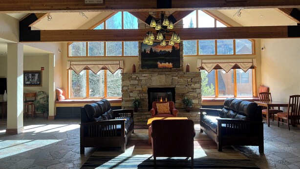 A spacious living room with a stone fireplace, leather sofas, and large windows offering views of the outdoors. - Charming Mountain Studio/ Walk to the Lifts (Keystone)
