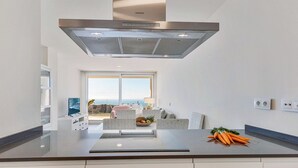 Een moderne keuken met een roestvrijstalen afzuigkap, een groot raam met uitzicht op de oceaan en een eethoek met rieten meubilair.