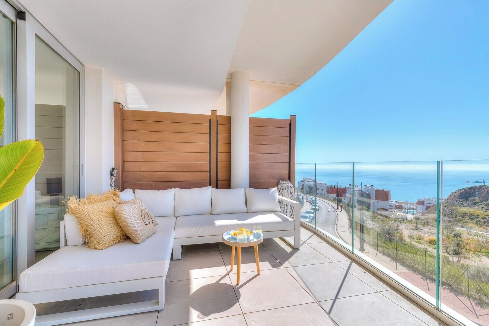 A balcony with a white sofa, a small table, and a view of the ocean.