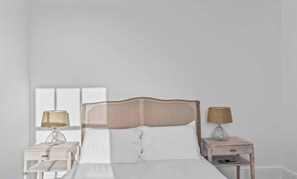 Un letto con testiera intrecciata, due comodini con lampade e una finestra sullo sfondo.