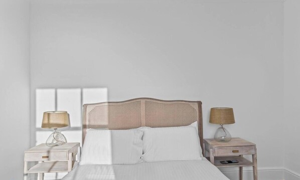 A bed with a woven headboard, two bedside tables with lamps, and a window in the background.