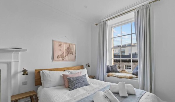 A bedroom with a bed, a nightstand, a wall-mounted lamp, a window with curtains, and a map on the wall.