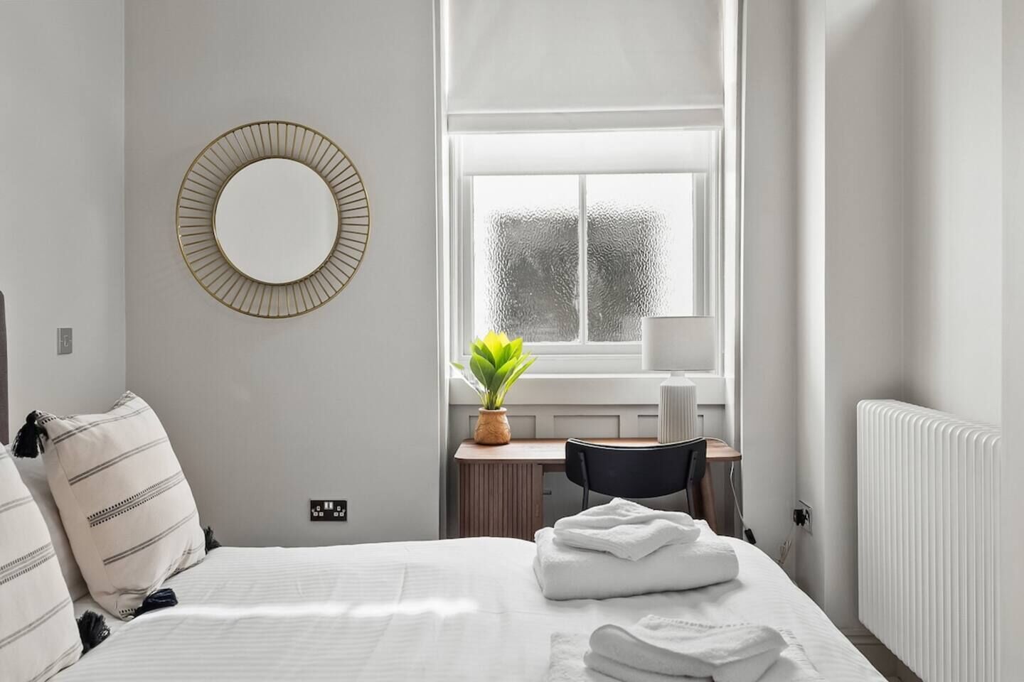 Une chambre à coucher comprenant un lit, un bureau, une chaise, une plante en pot et une fenêtre avec des stores.