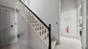 A staircase with white walls and a black handrail, leading to a landing with a fire extinguisher mounted on the wall. - Hurlingham by Pureserviced (Plymouth)