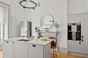A modern kitchen with a central island, a built-in oven, and a large window. - Hurlingham by Pureserviced (Plymouth)