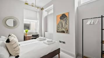 A modern bedroom with a bed, bedside table, mirror, artwork, and a clothing rack.