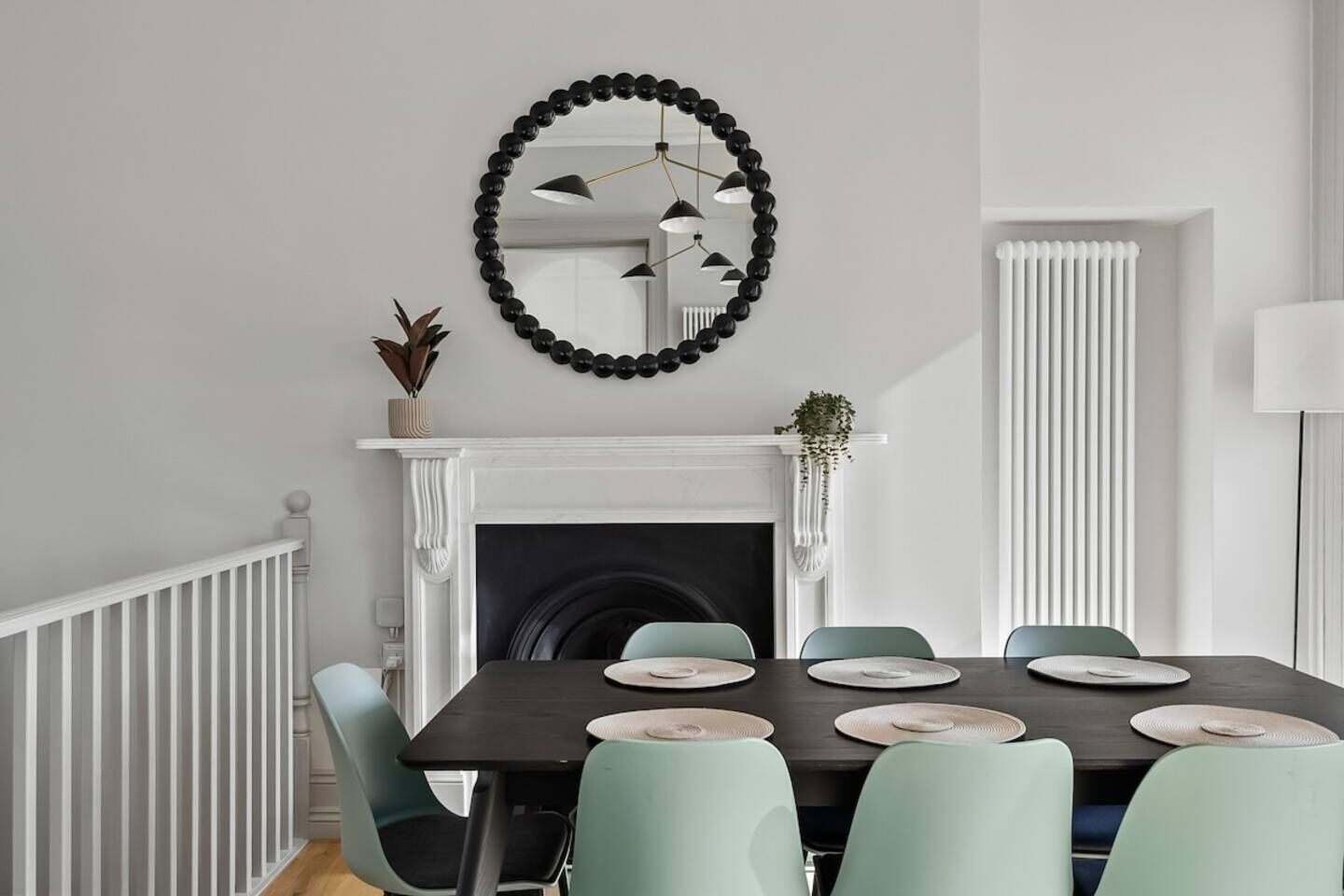 A dining room with a fireplace, a round mirror, and a radiator.