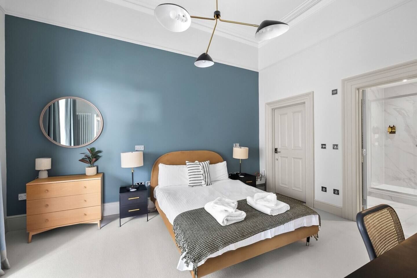 A hotel room with a bed, bedside tables, a dresser, a mirror, and a door.