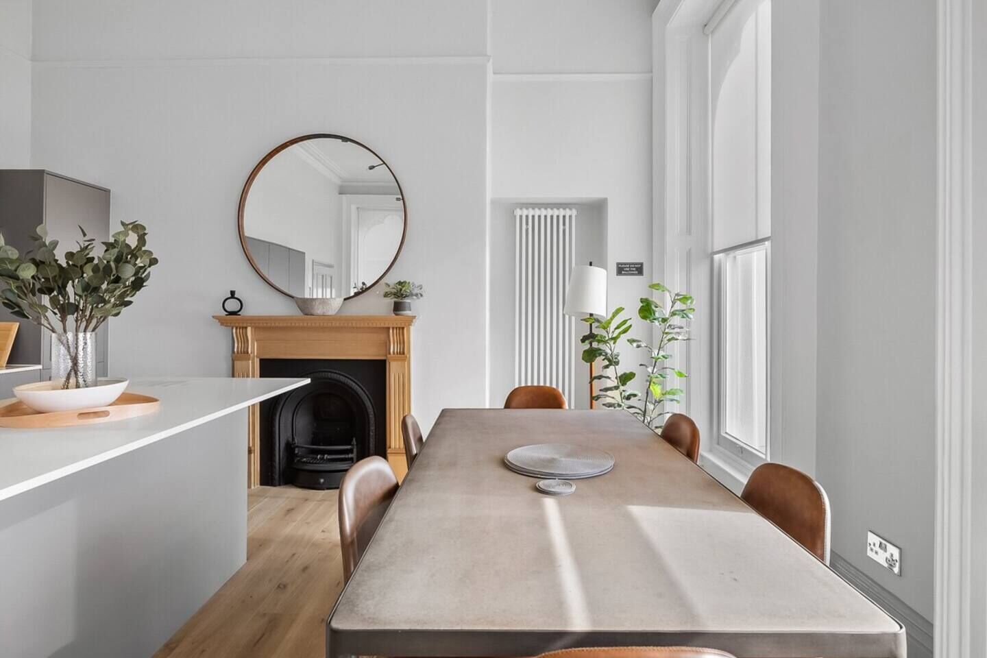 A dining area with a long table, chairs, a fireplace, and a large mirror.